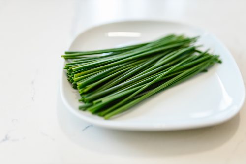 A close-up of fresh green chives neatly arranged on a white plate, showcasing a vibrant culinary ingredient.